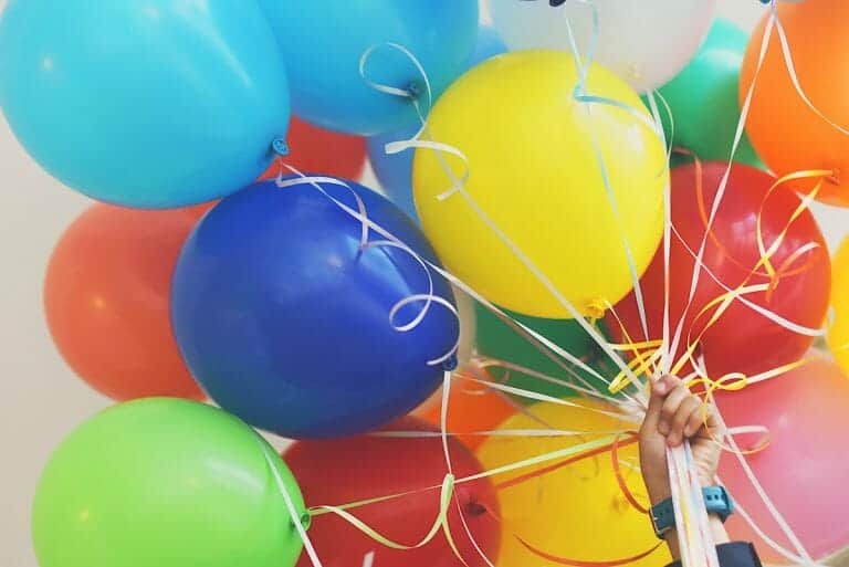 A child's hand holds a bunch of colorful balloons, celebrating Patnotebook's 10th anniversary.